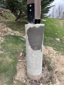 Concrete column base with carbon fiber reinforcement, partially finished installation, surrounded by grass and earth, showcasing structural support for StablWall projects.