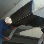 Worker applying carbon fiber reinforcement to a basement beam, showcasing foundation repair techniques for structural integrity and stability.
