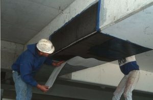 Technicians installing carbon fiber reinforcement sheet on concrete foundation beam